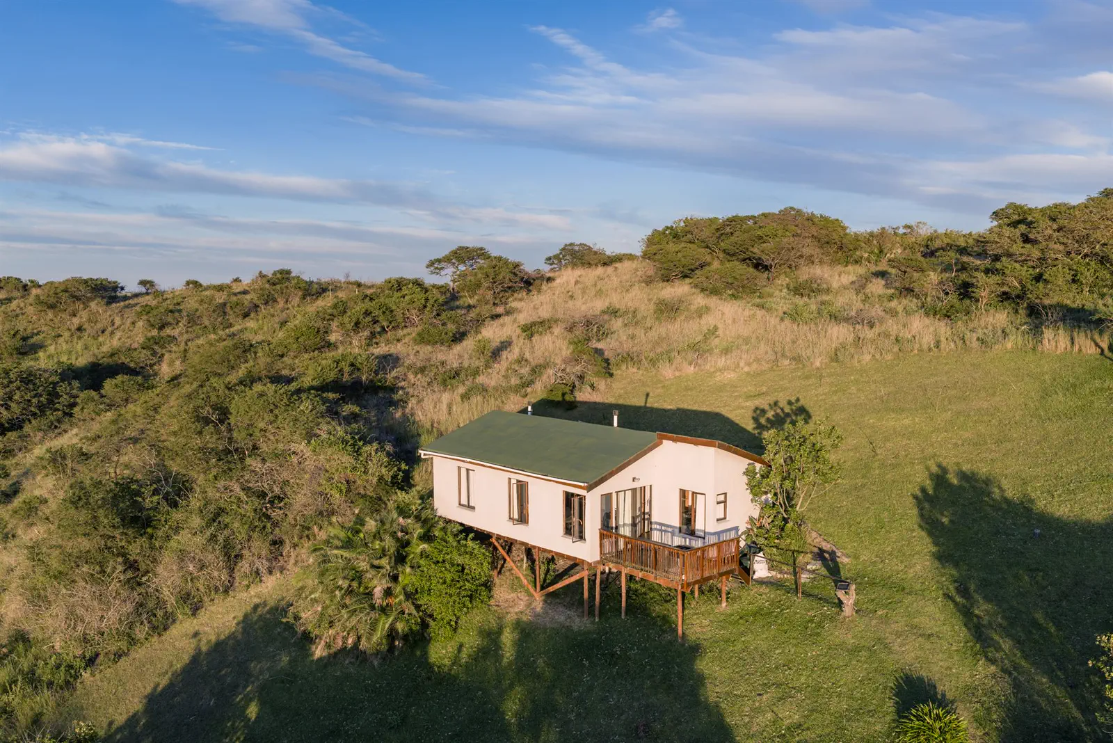 A cottage on stilts with a wooden deck, set in coastal bush