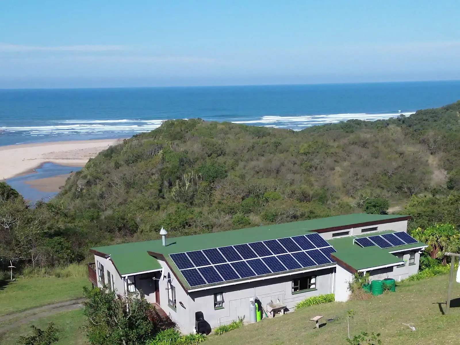 The Fish Eagle main house with solar panels on its green roof, the river mouth, beach and ocean behind