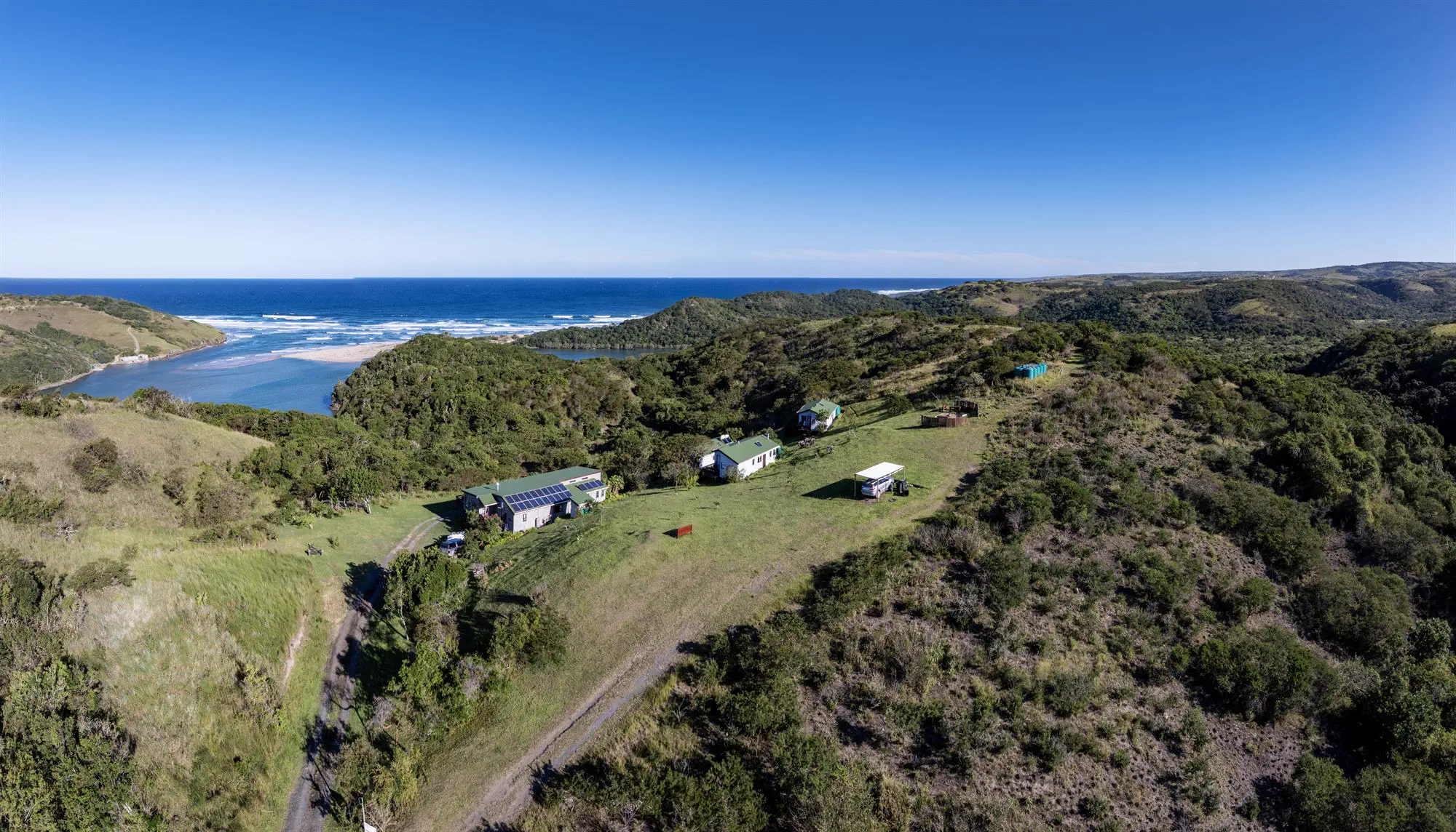 The lodge cottages on a green hilltop, with the river mouth and the Indian Ocean behind